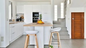A modern kitchen with white cabinetry, a wooden countertop, and two white bar stools.