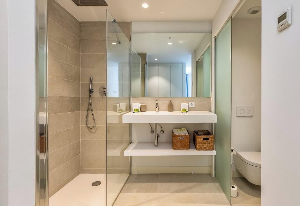 Un bagno moderno con box doccia in vetro, lavabo bianco con due specchi e un water.