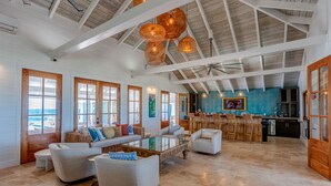 A spacious living area with a high ceiling, large windows, and a dining area with wooden chairs and a table. - Elbow Reef (Hope Town)