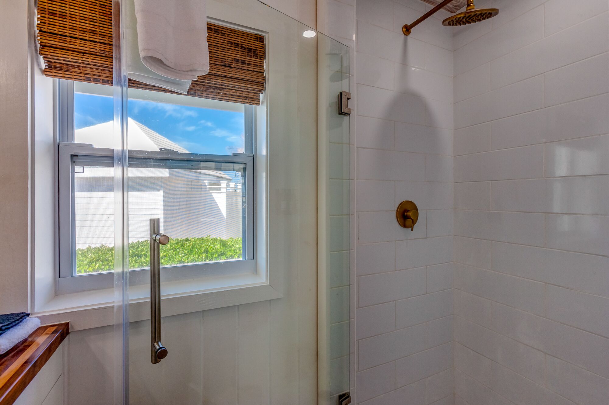 Een moderne badkamer met een douchecabine van glas, een raam met zonwering en uitzicht op een huis.