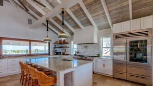 A spacious kitchen with a large island, white cabinetry, stainless steel appliances, and a view to the outside. - Elbow Reef (Hope Town)