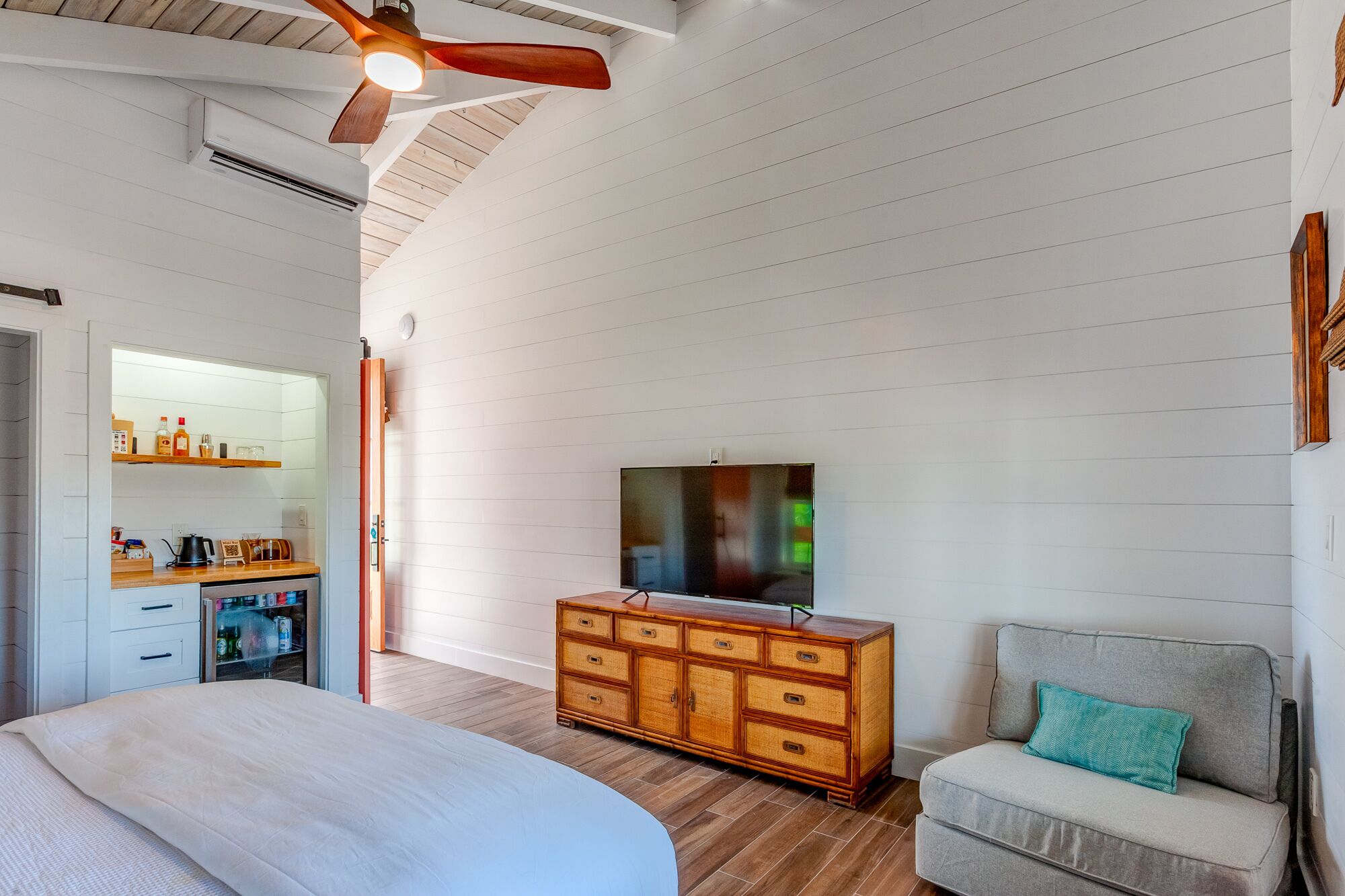Un dormitorio con una cama, un aparador de madera, un televisor y un sofá gris.