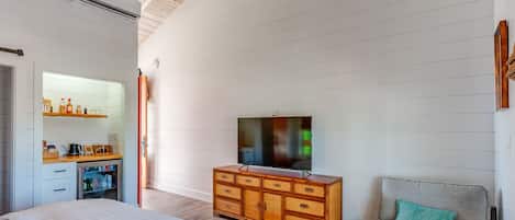 A bedroom with a bed, a wooden dresser, a television, and a gray sofa.