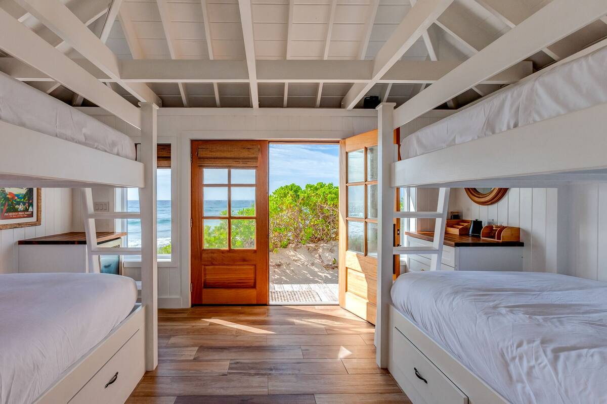 Un dormitorio con dos camas, una puerta de madera que da a un balcón y vistas al océano.