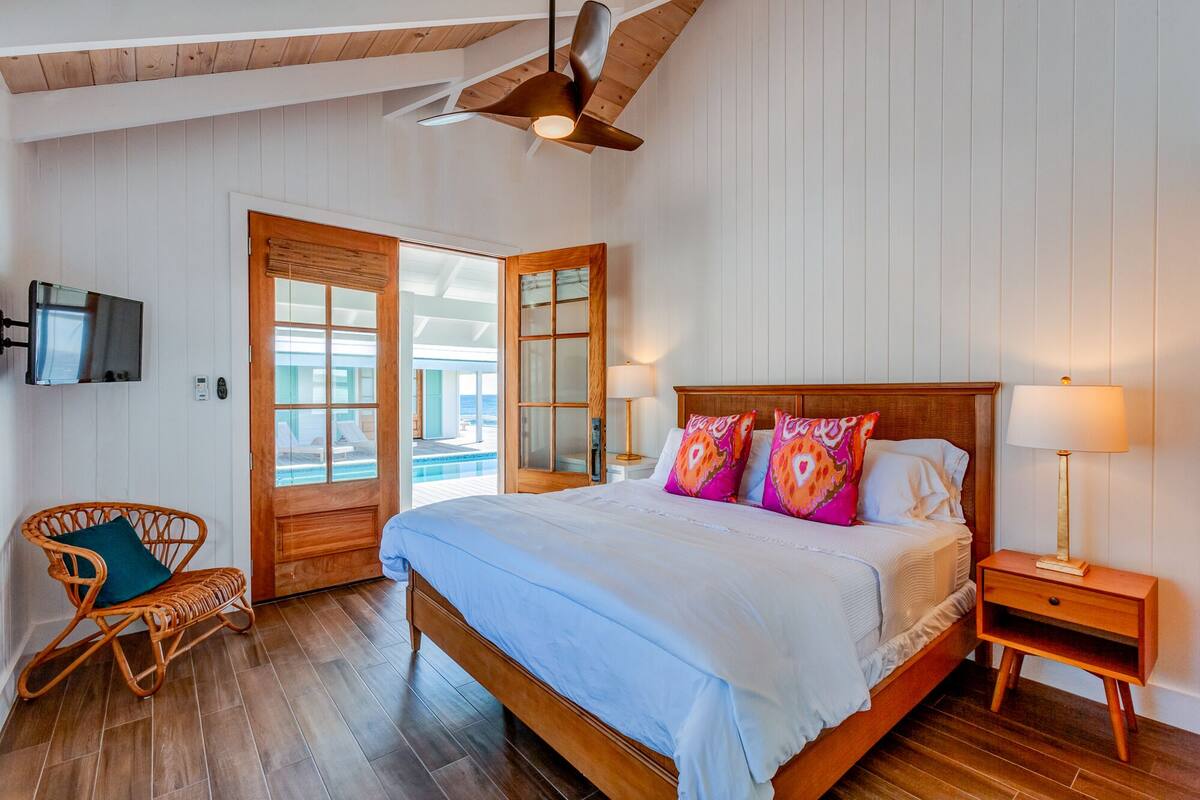 Un dormitorio con cama de madera, televisor en la pared y vista a la piscina a través de un ventanal.