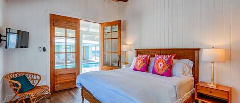 Ein Schlafzimmer mit einem hölzernen Bett, einem an der Wand montierten Fernseher und Blick auf den Pool durch eine Glastür.