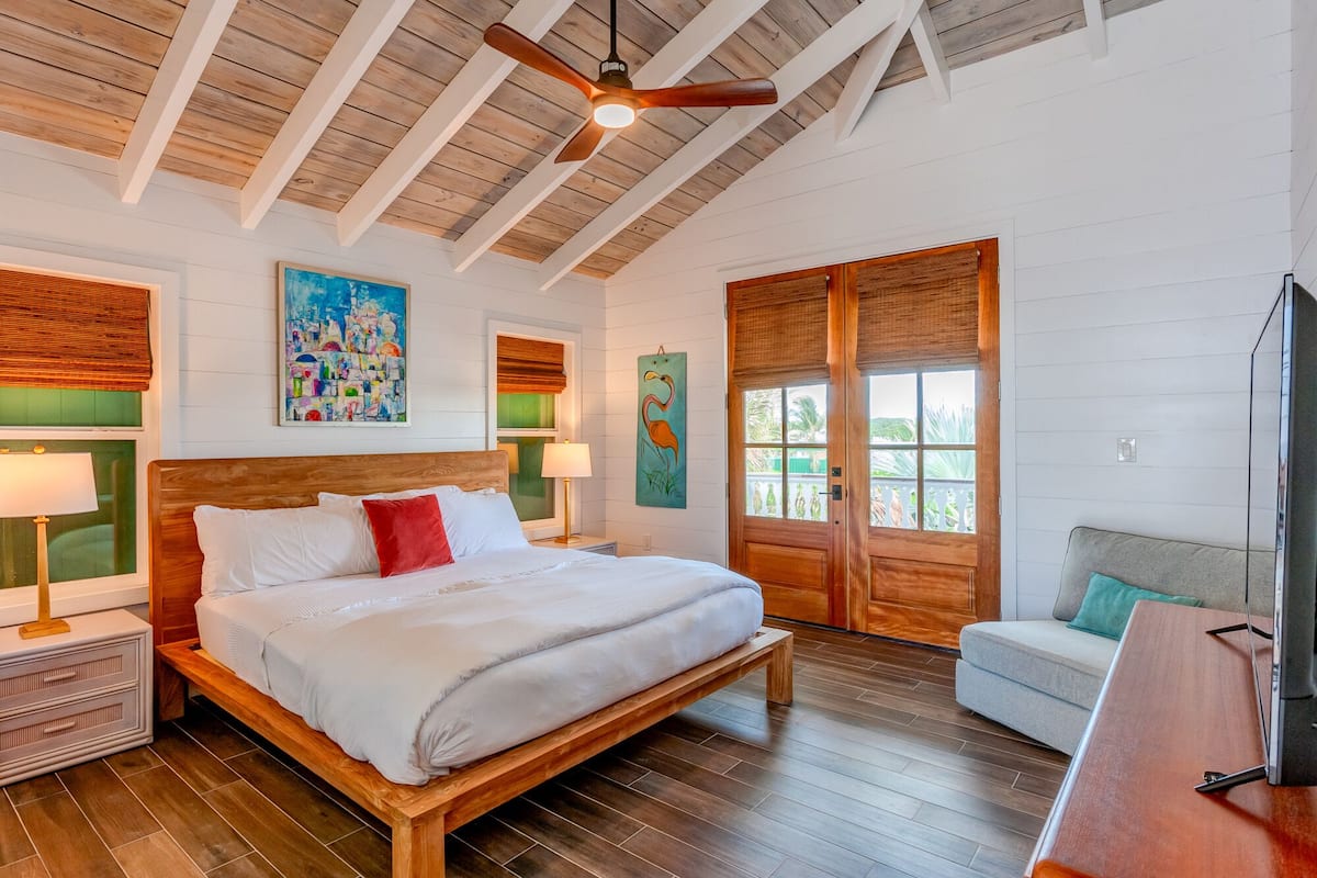 Un dormitorio espacioso con una cama de madera, ventilador de techo y un gran ventanal con vistas a palmeras.