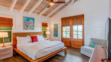 Un dormitorio espacioso con una cama de madera, ventilador de techo y un gran ventanal con vistas a palmeras.