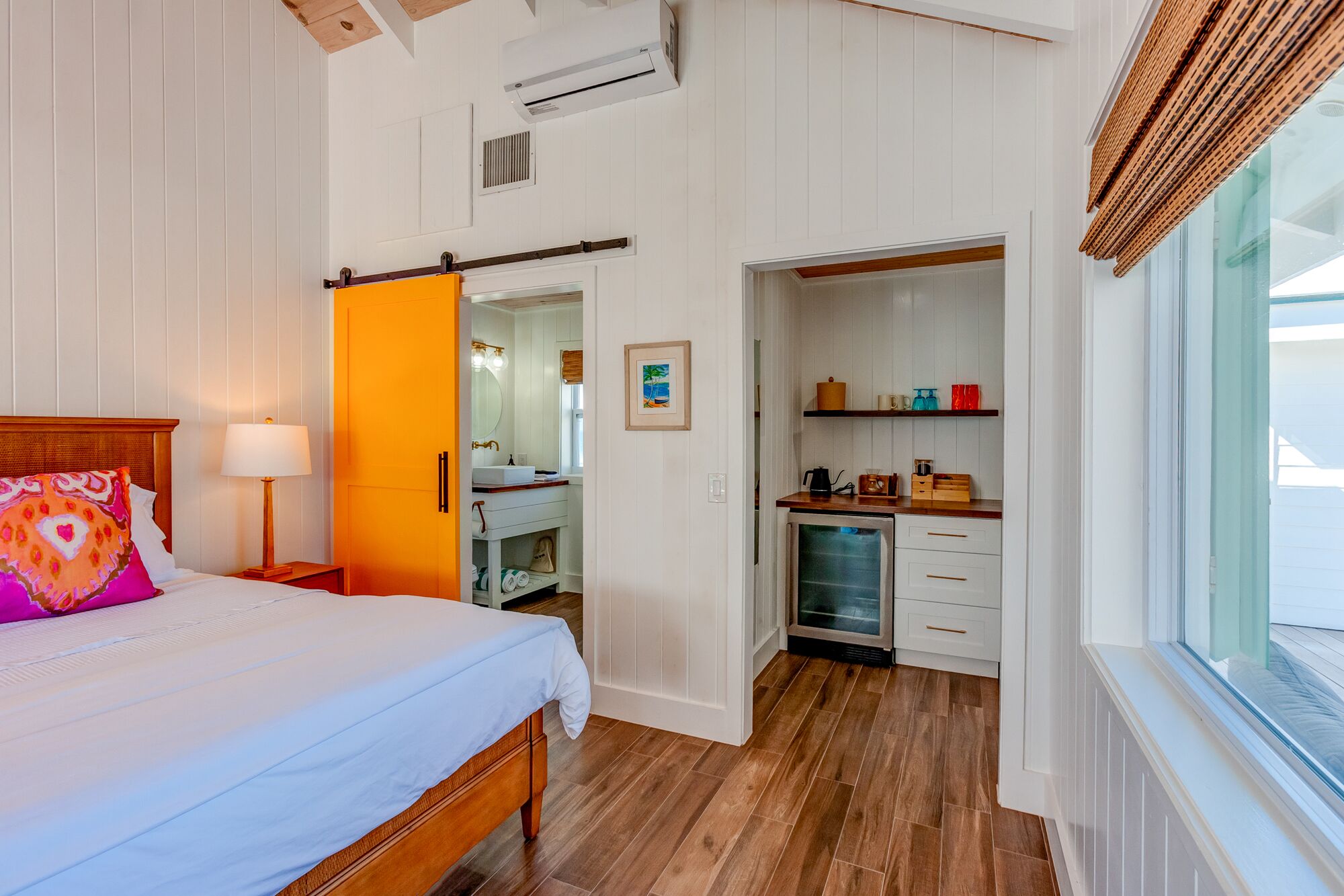 A bedroom with a bed, a nightstand, a lamp, a bathroom with a sink, mirror, and towel rack.