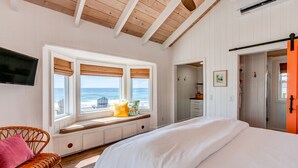 A bedroom with a large bed, a window seat with a view of the ocean, and a wicker chair. - Elbow Reef (Hope Town)