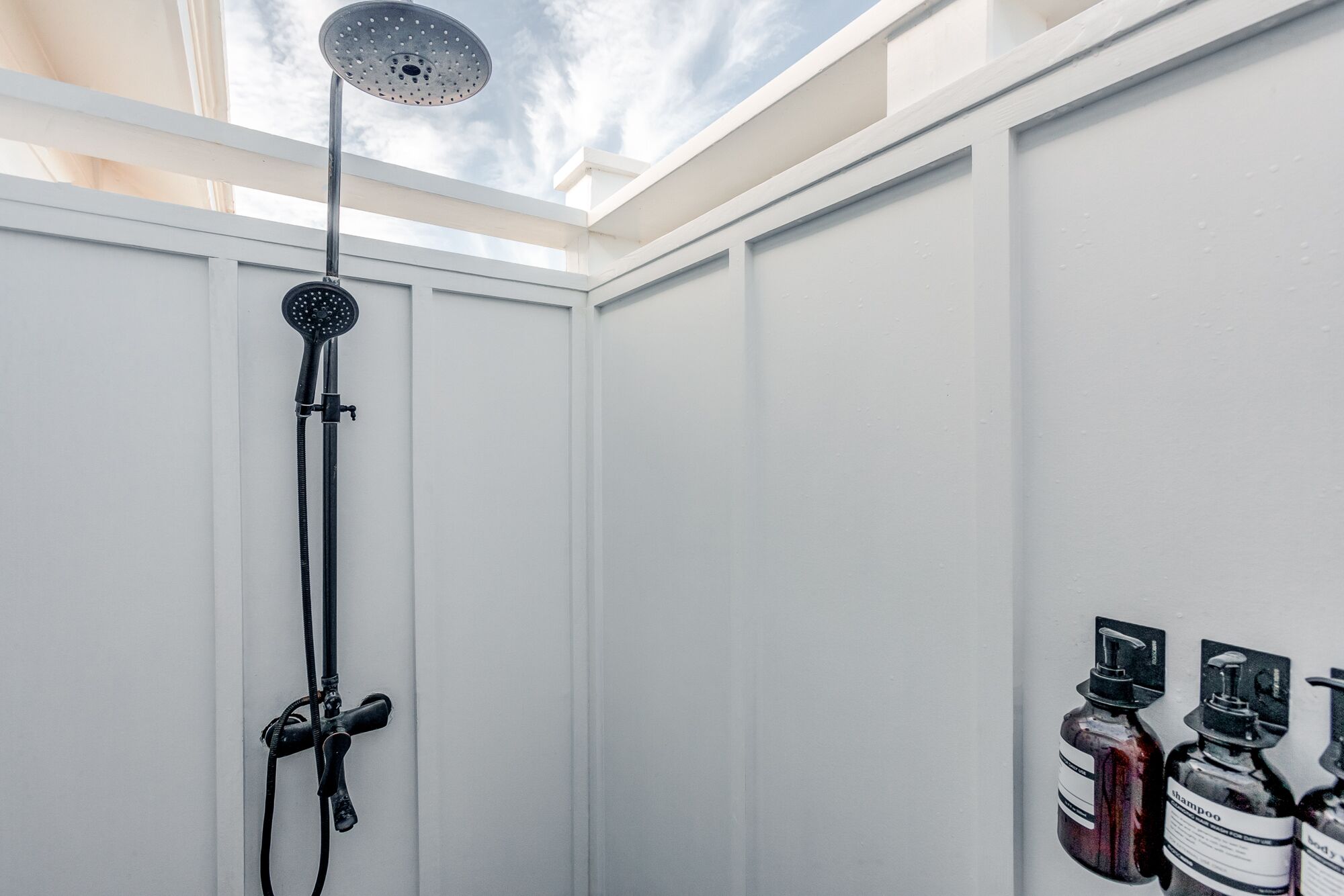 A shower with a rain showerhead and handheld showerhead, a skylight, and two bottles of shampoo and conditioner on the wall.