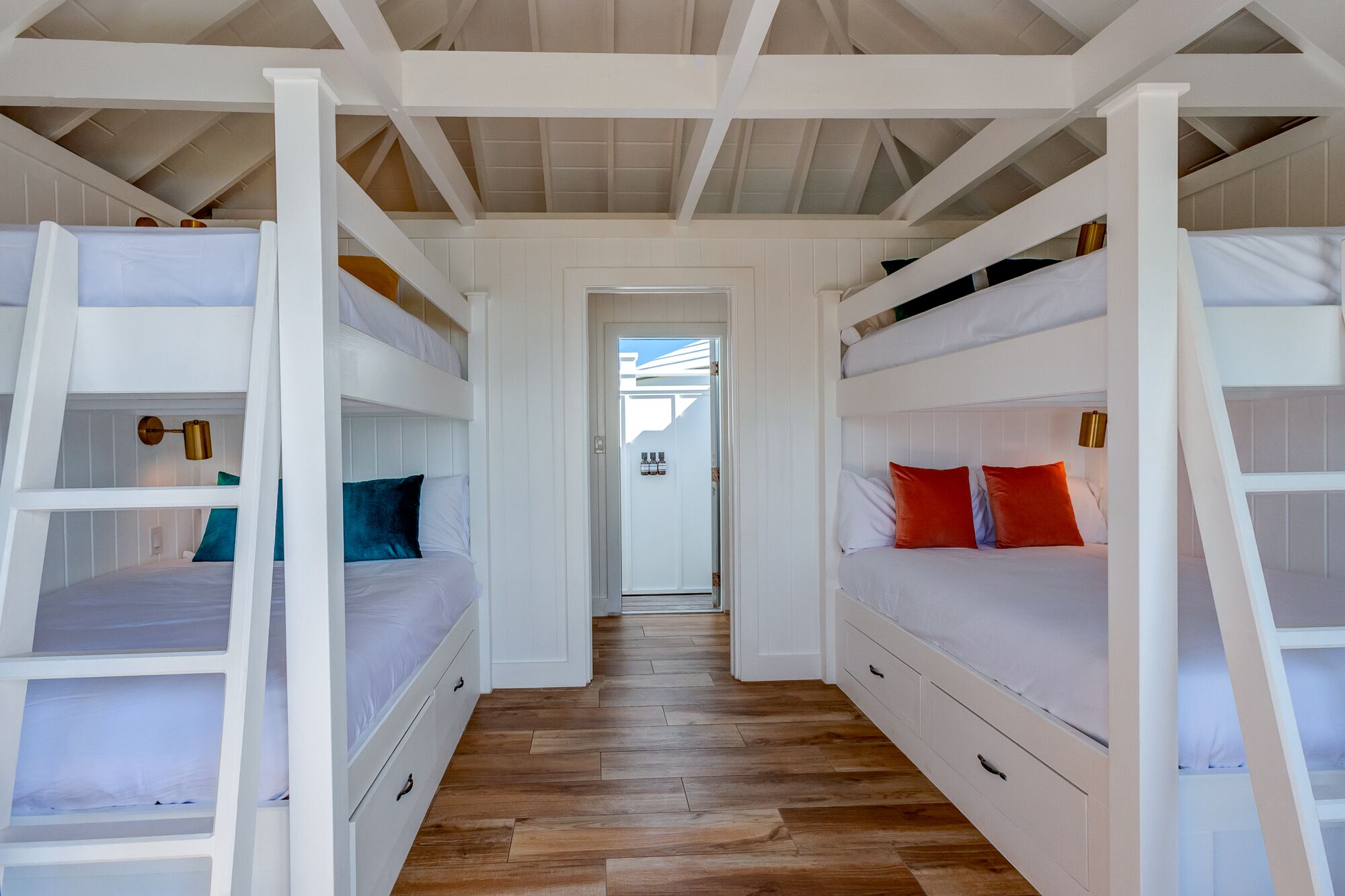 A room with bunk beds, wooden flooring, and a white door.