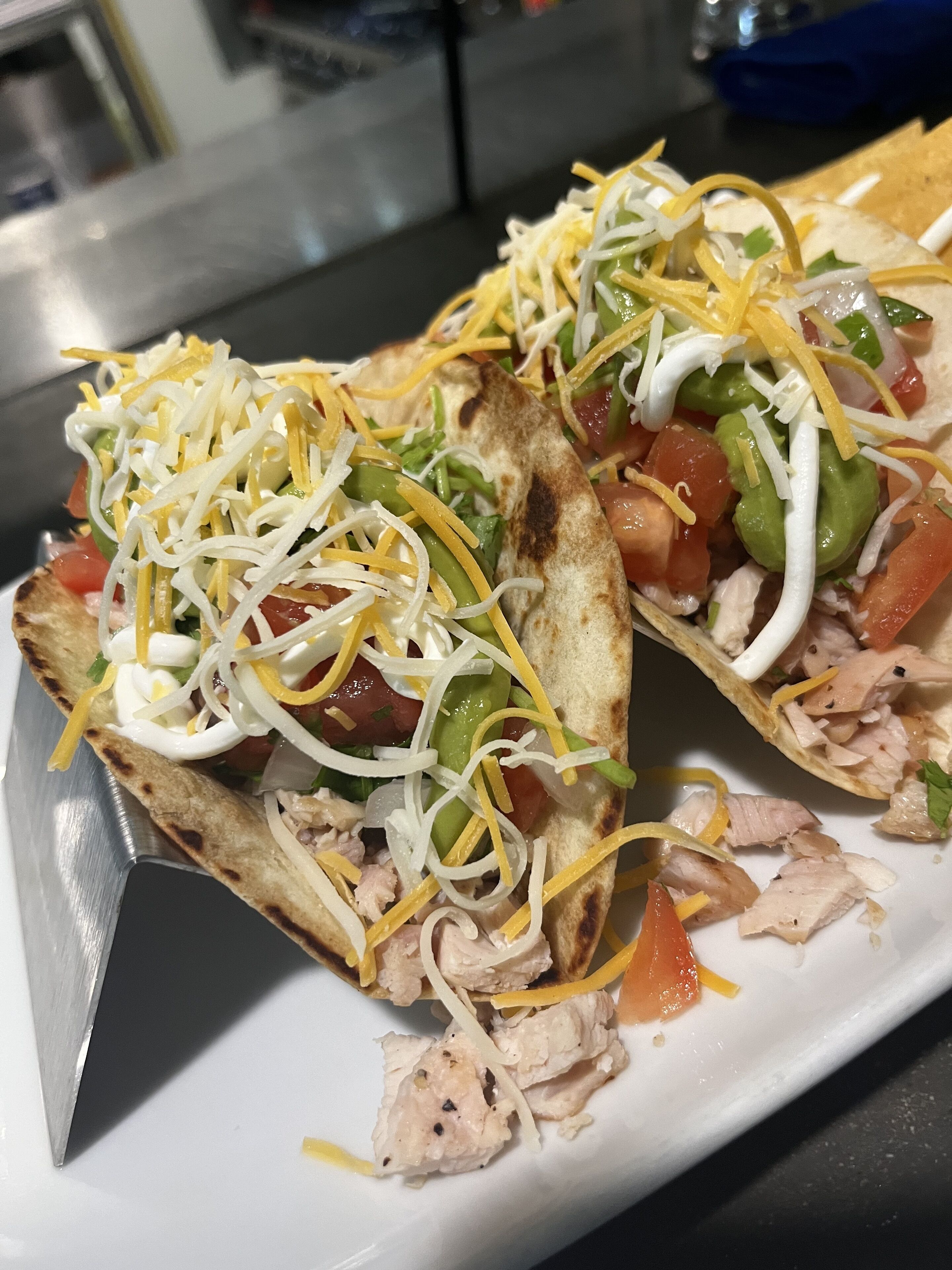 Twee taco's met geraspte kaas, blokjes tomaat en sla op een wit bord.