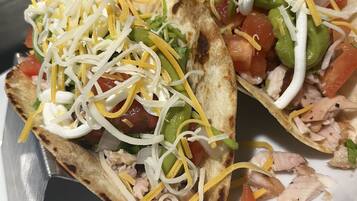 Twee taco's met geraspte kaas, blokjes tomaat en sla op een wit bord.
