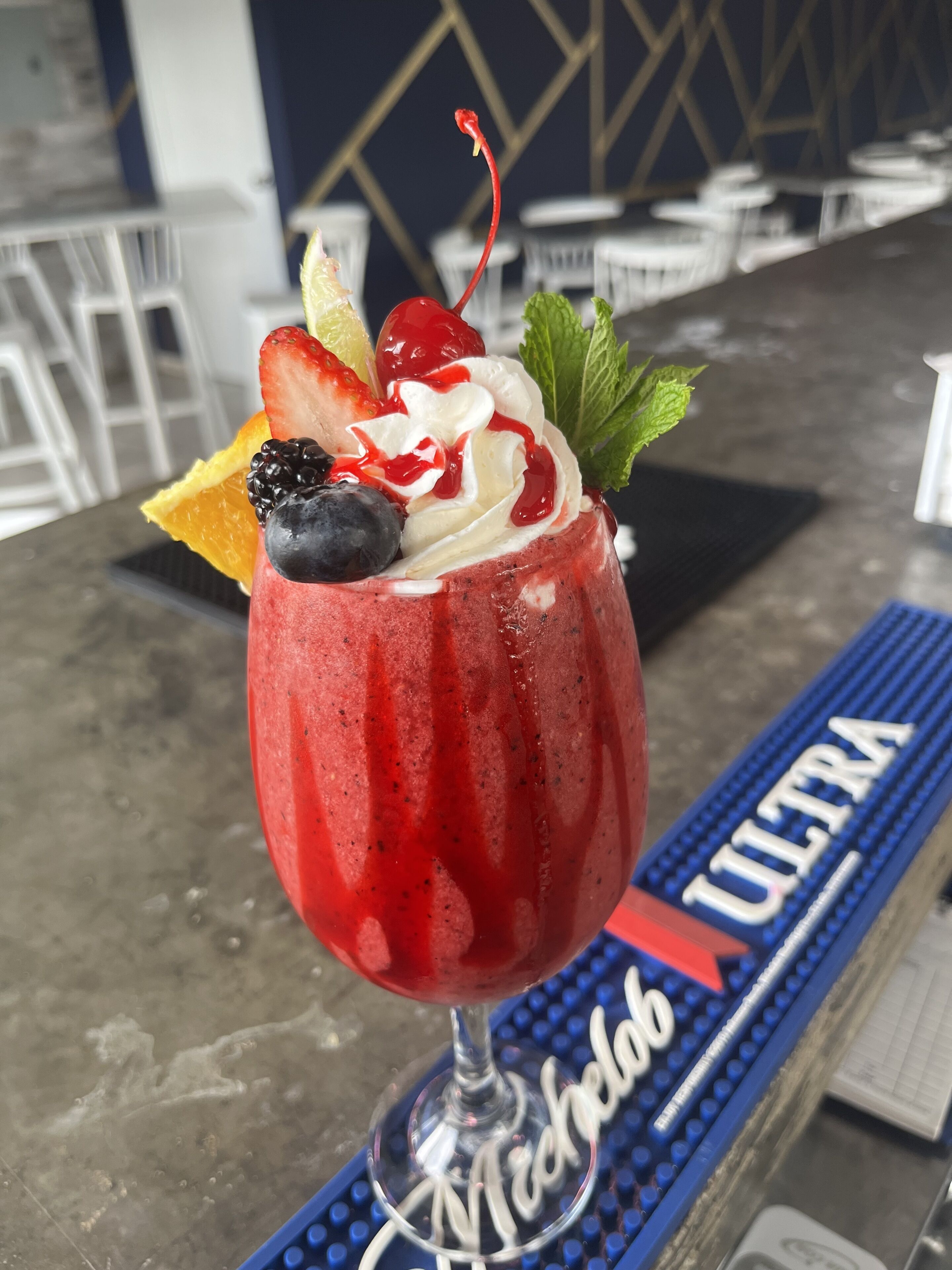 A cocktail with fruit garnish on a bar mat labeled "ULTRA" in a bar setting.