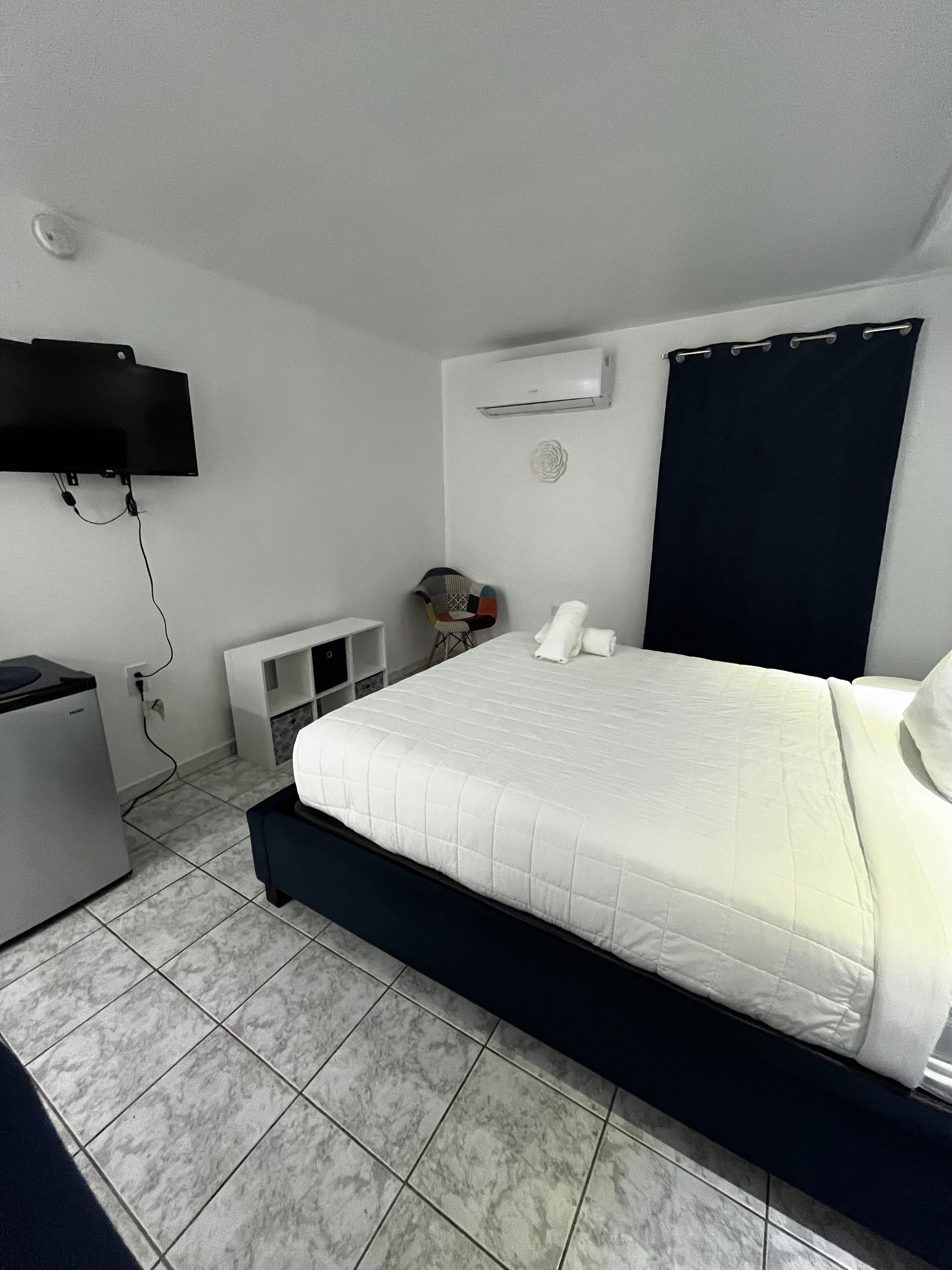 Quarto de hotel com cama, televisão na parede, aquecedor e uma pequena mesa com cadeira.
