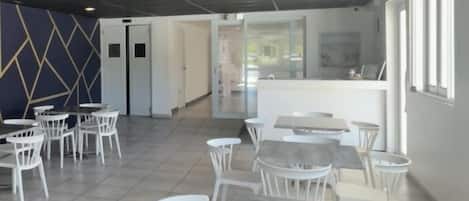 Een ruime binnenzone met witte stoelen en tafels, een receptiebalie en een modern plafondontwerp.