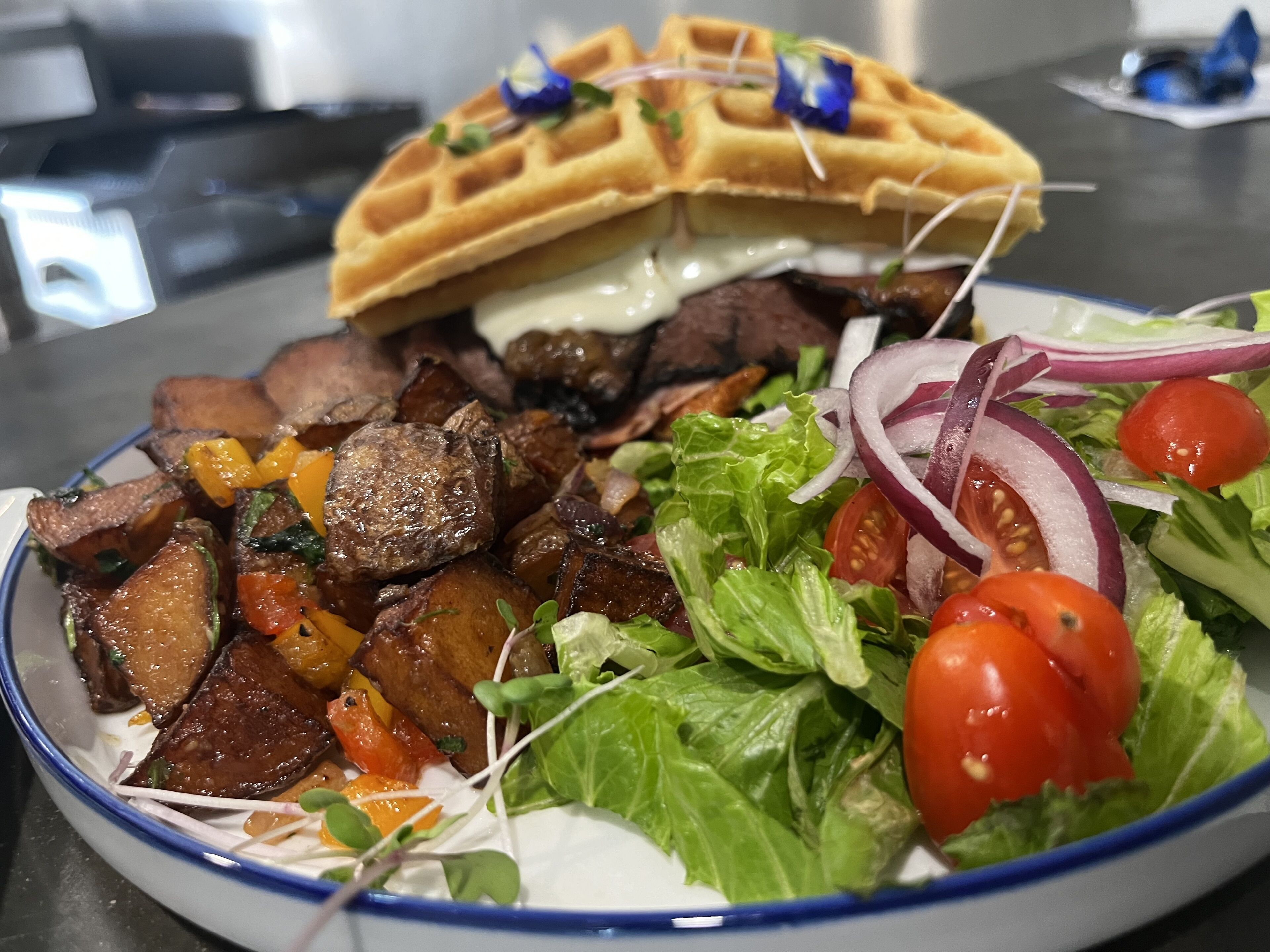 A plate of food with a waffle, meat, vegetables, and a salad.