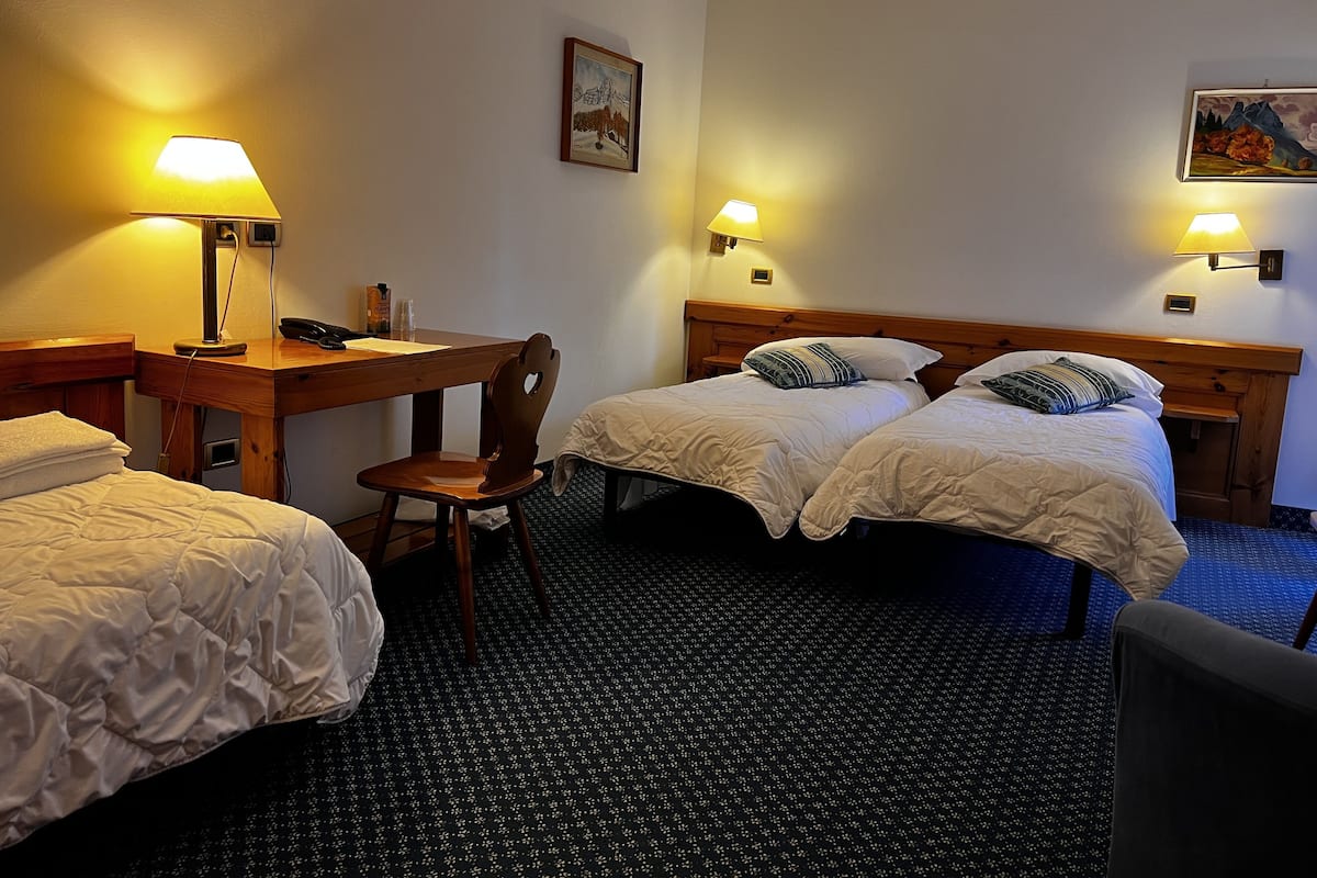 A hotel room with two beds, a desk, a chair, and two wall-mounted lamps.