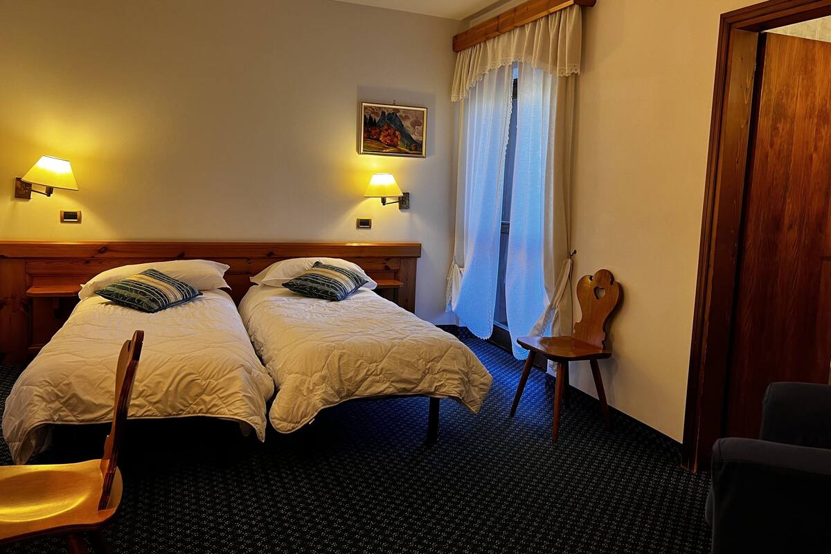 A hotel room with two beds, a desk, a chair, a lamp, and a painting on the wall.