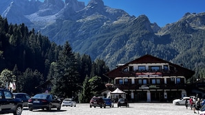 A mountain lodge with a sign welcoming runners, surrounded by forested mountains and parked cars. - Hotel Bosco Verde (Val di Zoldo)