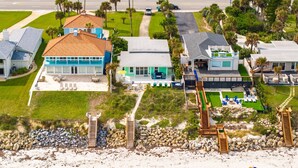 Une propriété située sur la côte, comprenant plusieurs maisons, une plage de sable et un sentier menant à un espace piscine.