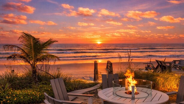 Un espace de plage aménagé avec un coin salon extérieur circulaire, un foyer et une vue sur l’océan au coucher du soleil.