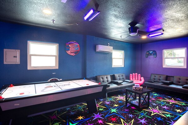 A room with a foosball table, a couch, and a neon sign. - 🌊 A1A Oceanfront Beach House | Hot Tub, Game Room, Pet Friendly 🐾 (Daytona Beach)