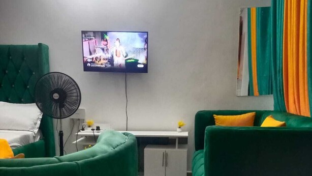 Ein Zimmer mit einem grünen Sofa, einem weißen Nachttisch, einem an der Wand montierten Flachbildfernseher und einer kleinen weißen Kommode.