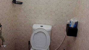 Ein kleines Badezimmer mit Fliesen, einer Toilette, einem Fenster und einem Ablagefach für Toilettenartikel.
