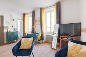 A modern living room with a sofa, a television, and a dining area with a table and chairs.