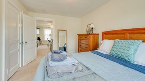 Een slaapkamer met een bed, een houten dressoir, een spiegel en een deur die naar een andere kamer leidt.