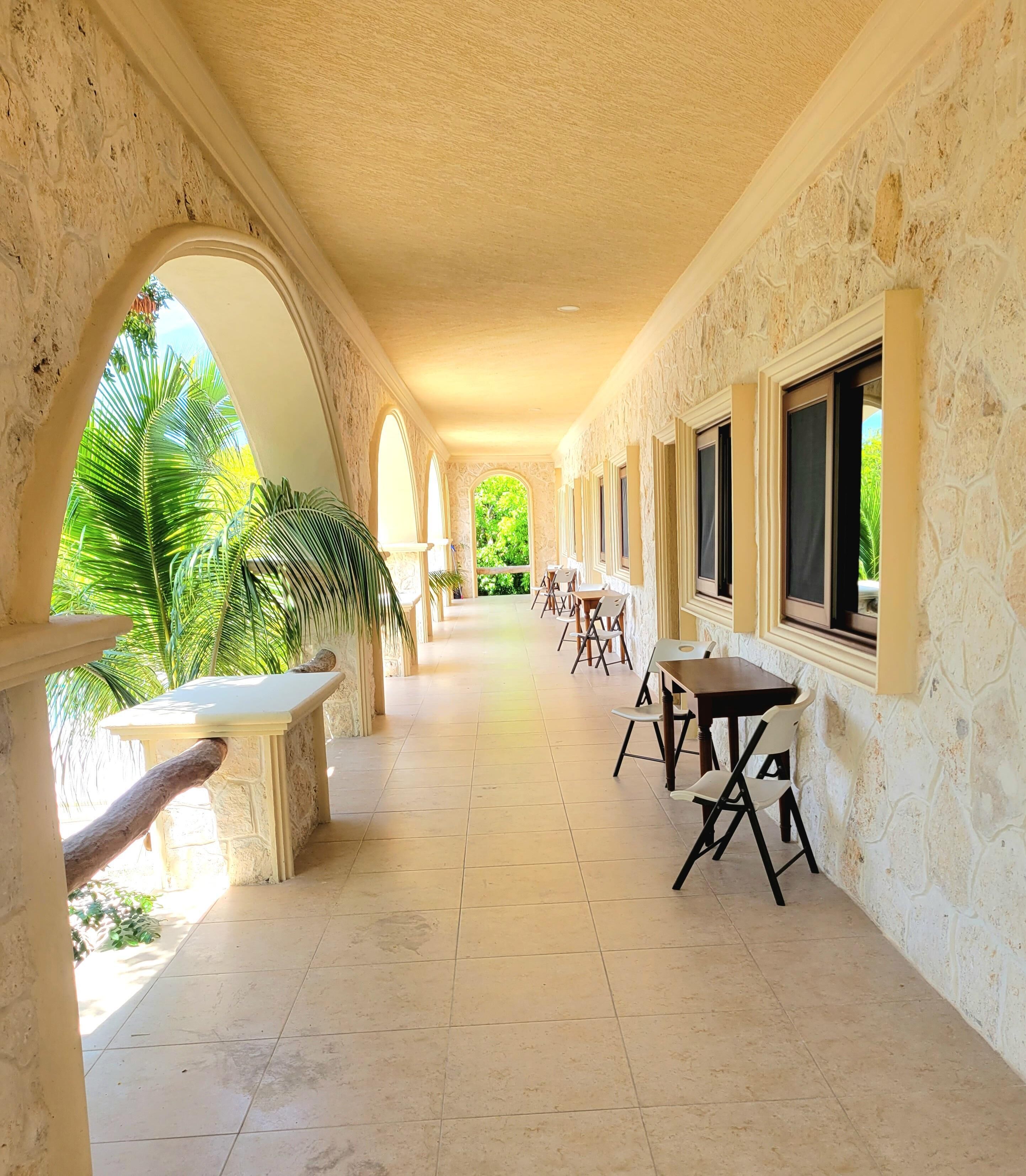Un couloir orné d’arches, doté d’un sol carrelé, et où des tables et des chaises sont disposées le long des murs.