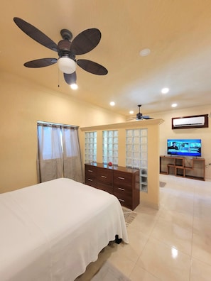 A hotel room with a bed, a ceiling fan, a TV, and a window with curtains.