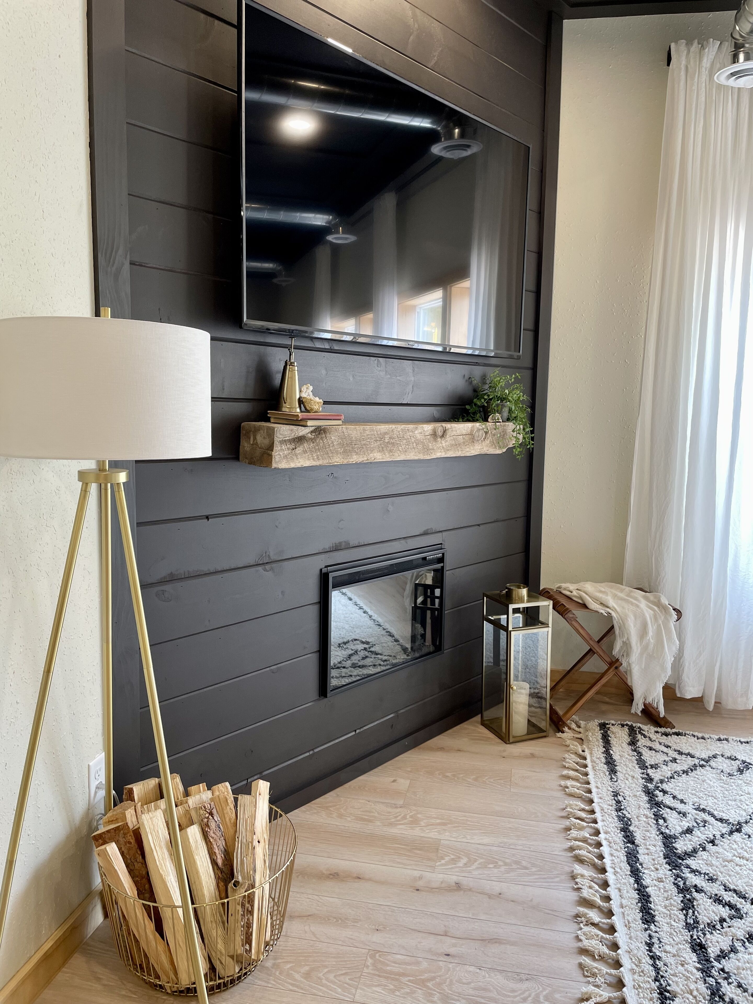 A modern living room with a fireplace, wooden shelves, a floor lamp, and a patterned rug.