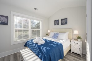 A bedroom with a large bed, white nightstands, a window with blinds, and two wall-mounted artworks. - 4 Luxury Home w/ Pool, FirePit, Outdoor Dining,| The Marshes Broad View (Hilton Head Island)