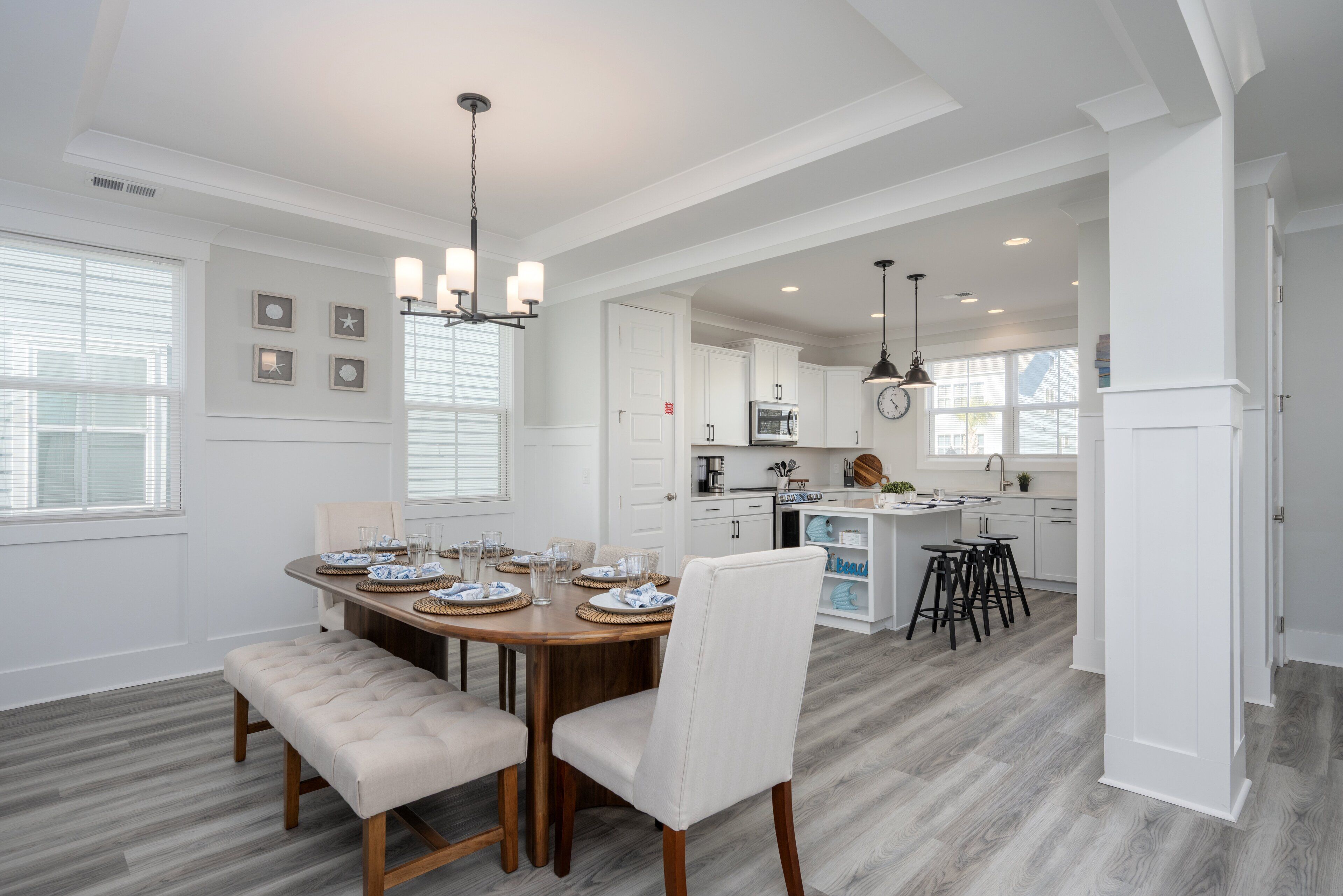 A spacious dining area with a wooden table set for four, a bench, and a chandelier.
