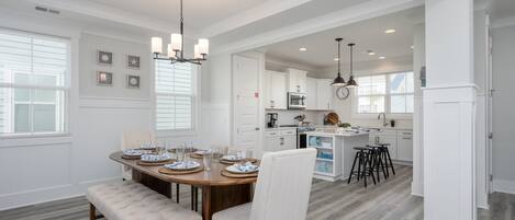 A spacious dining area with a wooden table set for four, a bench, and a chandelier.
