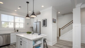 A modern kitchen with white cabinetry, a stainless steel refrigerator, pendant lighting, and a wooden staircase. - 4 Luxury Home w/ Pool, FirePit, Outdoor Dining,| The Marshes Broad View (Hilton Head Island)