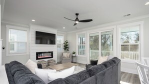 A modern living room with a grey sofa, a coffee table, and a flat-screen TV mounted on the wall. - 4 Luxury Home w/ Pool, FirePit, Outdoor Dining,| The Marshes Broad View (Hilton Head Island)