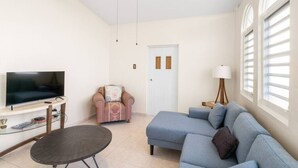 A living room with a flat-screen TV, a sofa, a chair, a lamp, and a small table.