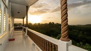 A balcony with a view of a sunset over a hilly landscape.