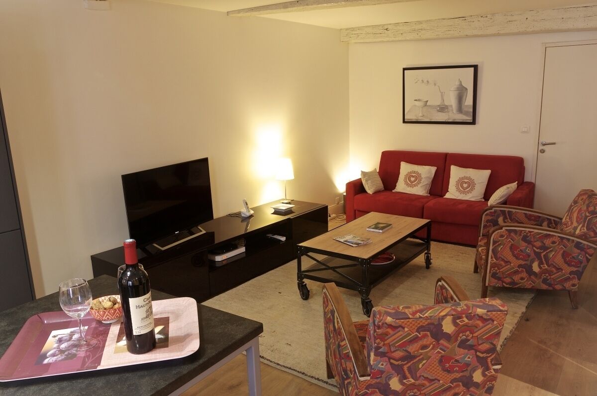 A living room with a red sofa, patterned armchairs, a coffee table, a TV, and a wine bottle on a tray.