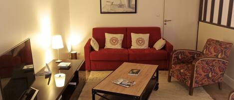 Una sala de estar con un sofá rojo, un sillón estampado y una mesa de centro.