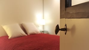A bedroom with a red bedspread, a white wall, and a nightstand with a lamp. - Sauvageau - 1 chambre avec parking (Burdeos)