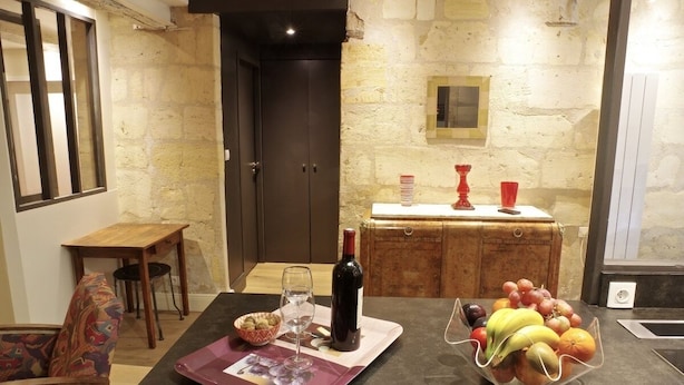 A dining area with a table set for two, a wine bottle, and a fruit bowl. - Sauvageau - 1 chambre avec parking (Burdeos)