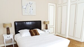 A neatly made bed with white linens and a brown throw pillow, flanked by two bedside tables with lamps, in a room with wooden flooring and a large wardrobe. - Louis Combes - Localisation Exceptionnelle / 1 cha (Burdeos)