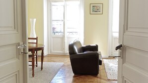 A room with a wooden chair, a black leather sofa, a white door, and a window with a view of the outside. - Louis Combes - Localisation Exceptionnelle / 1 cha (Burdeos)