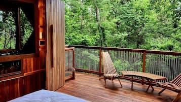 A wooden deck with two lounge chairs, a table, and a bar area with a view of the forest.