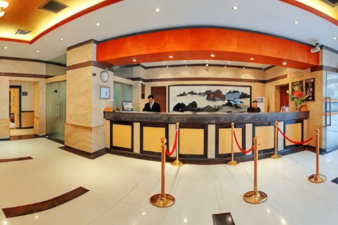 Balcão de recepção de hotel com recepcionista, um computador e um quadro na parede.
